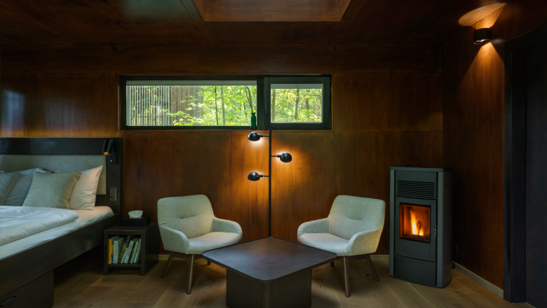 edelførst tree houses, © Robert Tober Interior view of a cozy tree house with wooden paneling, two armchairs, a table and a fireplace.