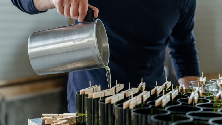 Candle manufactory, © Glaser Kerzen Person pours liquid from a metal container into candle molds.