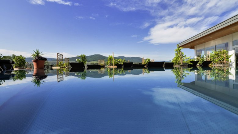 Penthouse spa with pool, © Alexander Pfeffel A modern pool on a penthouse with a view of the mountains and blue sky.