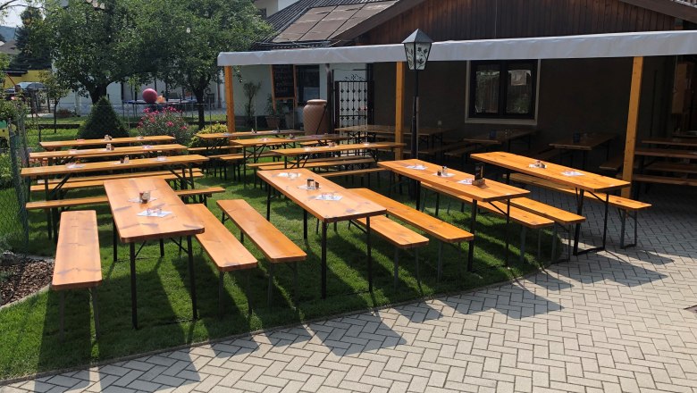 TDR-HeurigerBacherRoiser-Heurigengarten, © Ernst Roiser Wooden benches and tables in a wine tavern garden with sun protection.