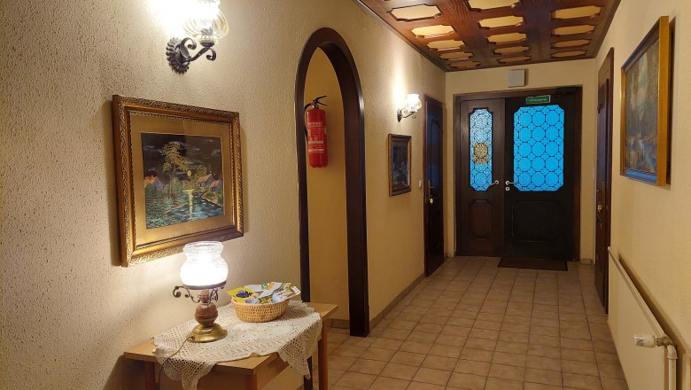 TDR-Welserhof inside, © Nora Bartfai Interior view of a hallway with wooden table, lamp, paintings and blue glass doors.