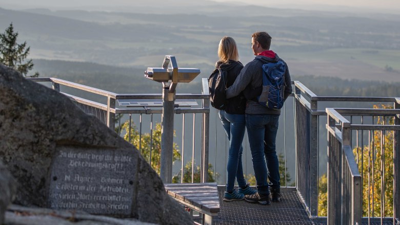 Hike on the Mandelstein, © Christian Freitag A couple stands on a viewing platform with a view of a vast landscape.