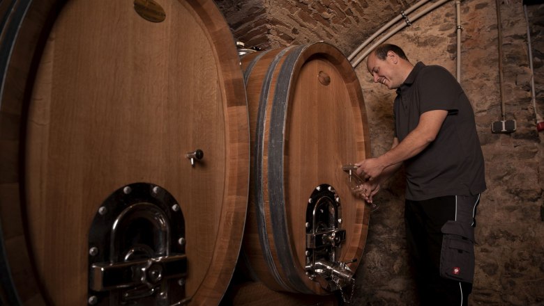 Wooden barrels_Christoph Donabaum, © Nimo Zimmerhackl A man draws wine from a large wooden barrel in a wine cellar.