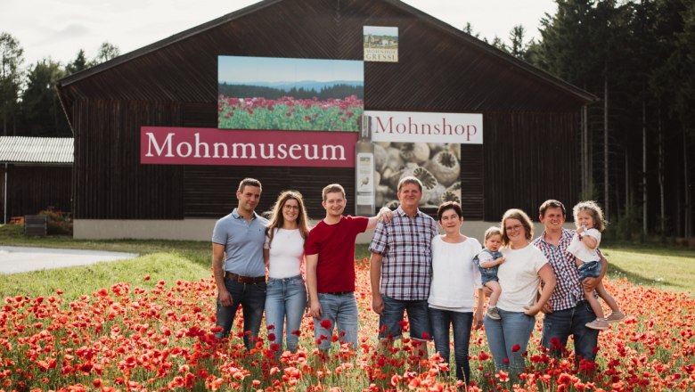 20230713karolinegrill_fam_gressl-hp, © Karoline Grill A family stands in a poppy field in front of a building labeled 'Poppy Museum'.