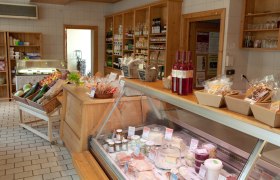 Schneebergland gourmet store, © Marktgemeinde Bad Fischau-Brunn, Fotograf Lukas Dostal Interior view of a delicatessen with wooden shelves, vegetables, bottles of wine and a refrigerated counter with cheese and spreads.