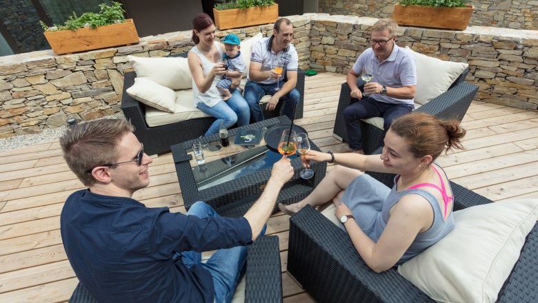 Social get-together on the terrace, © KASTNER NEW MEDIA - kastner.tv Group of people sitting aOn a terrace, toasting with drinks.