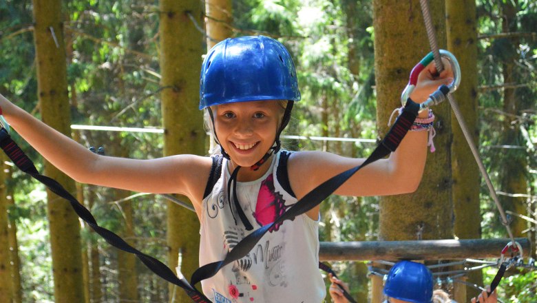 Skill on the course, © Hamari Kletterpark A girl in a blue helmet balances on a climbing course in the forest.