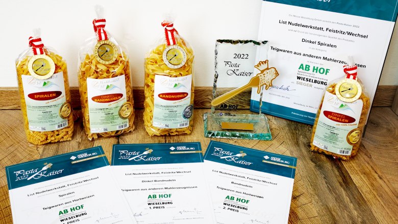 Pasta Kaiser 2022, © Familie List Various pasta packs and awards on a wooden floor.