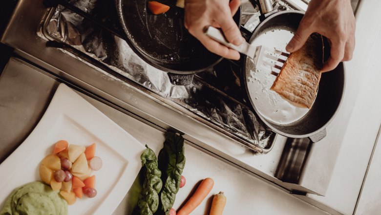 The kitchen line: reliable down-to-earthness with fresh ideas, © Niederösterreich Werbung/Rita Newman Chef prepares salmon in a pan, vegetables and puree on a plate next to it.