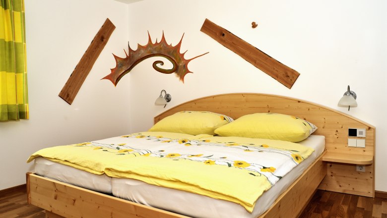 Rooms - Gasthof zur Kirche, © Gasthof zur Kirche A cozy bedroom with a wooden bed, yellow bed linen and decorative wooden elements on the wall.