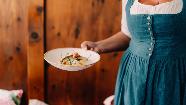 Toque-awarded restaurant with high-quality Austrian cuisine, © Niederösterreich Werbung/Julius Hirtzberger Woman in traditional costume serves a dish on a plate.