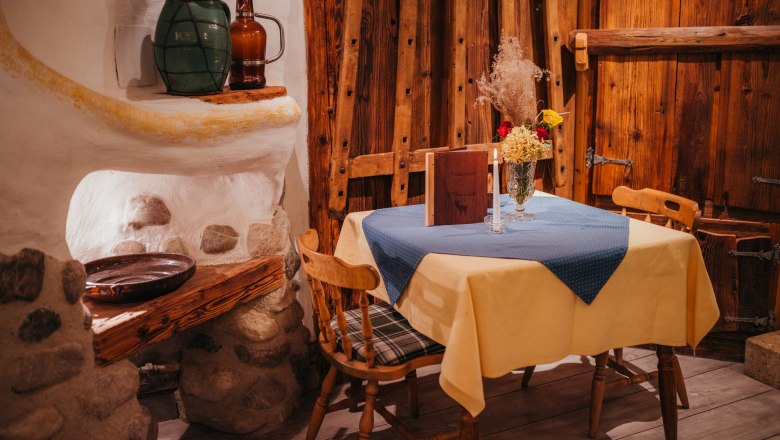 The farm has been an inn since 1977, © Niederösterreich Werbung/Daniela Führer Rustic inn interior with wooden furniture, table with yellow tablecloth, blue napkin, flowers and candle.