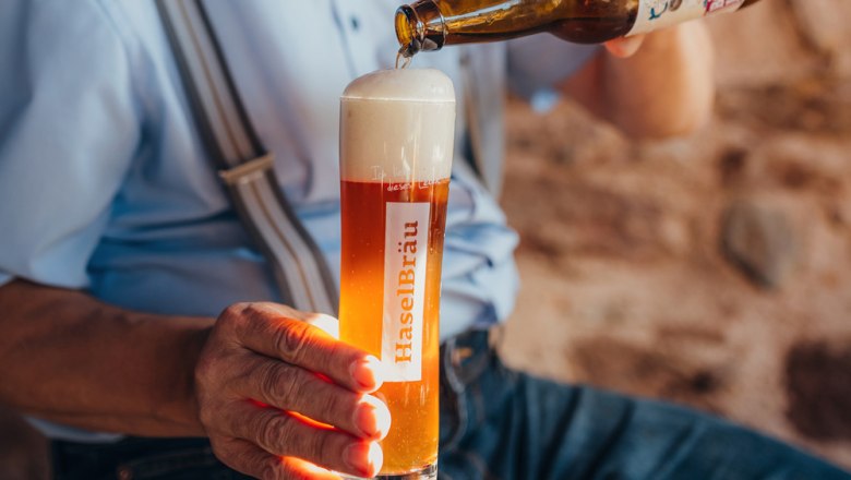 Home-brewed beer, © Niederösterreich Werbung/Daniela Führer A person pours beer from a bottle into a glass labeled 'HaselBräu'.