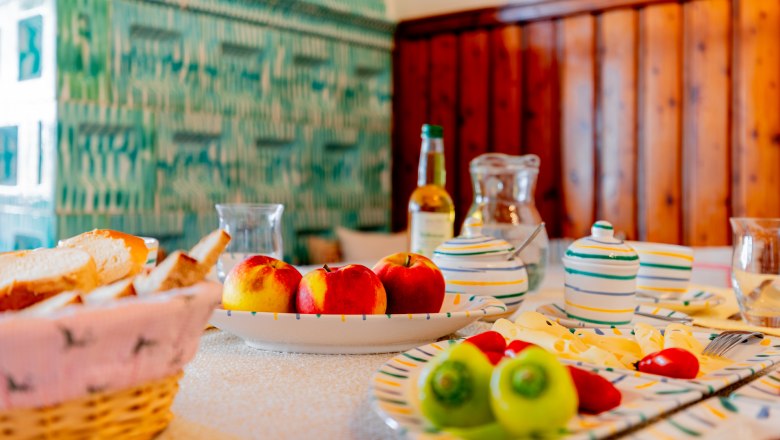 Woltron Manor, © Wiener Alpen / Christian Kremsl A table laid with fruit, bread and crockery in front of a green tiled wall.