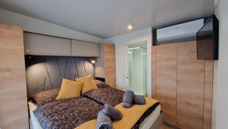 Double bed Johannesbachklamm Chalet, © Johannesbachklamm Chalet Interior view of a bedroom with double bed, yellow pillows and towels, wardrobe, air conditioning and view of the bathroom.