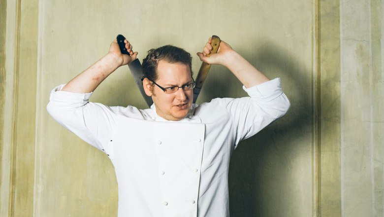 Chef Erwin Windhaber, © Hofmeisterei Hirtzberger/Julius Hirtzberger A man in chef's clothes holds two knives behind his head.