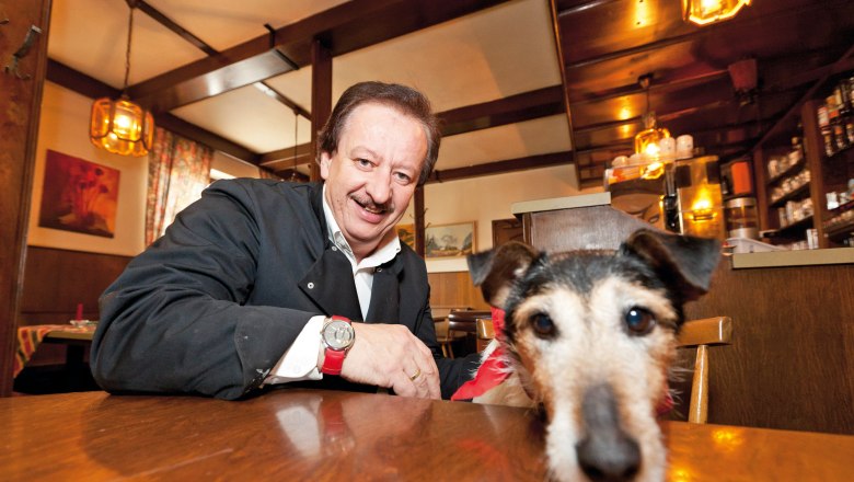 Country inn Riefenthaler, © Franz Riefenthaler A man in an inn smiles while a dog with a red bandana lies on the table.