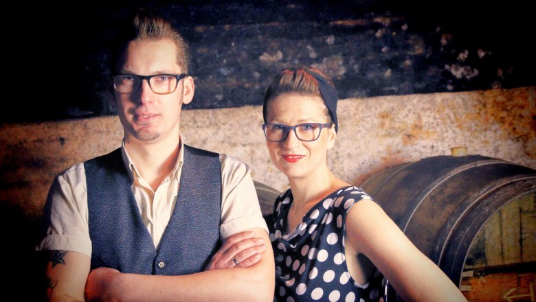 Pollak René and Ramona, © Matthias Karasek A man and a woman stand next to each other in front of a rustic background with a barrel.