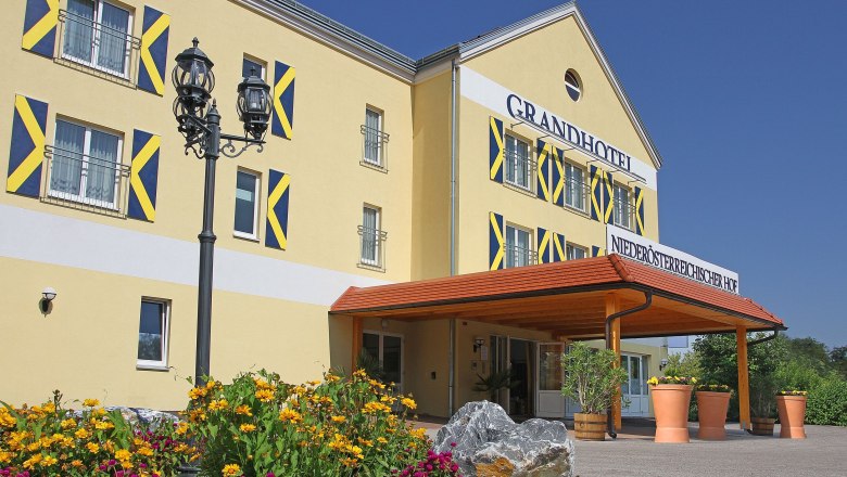 Wedding pavilion, © Besta Betriebs GmbH Exterior view of a yellow hotel with blue shutters and a canopy. Yellow and pink flowers bloom in front of the building.