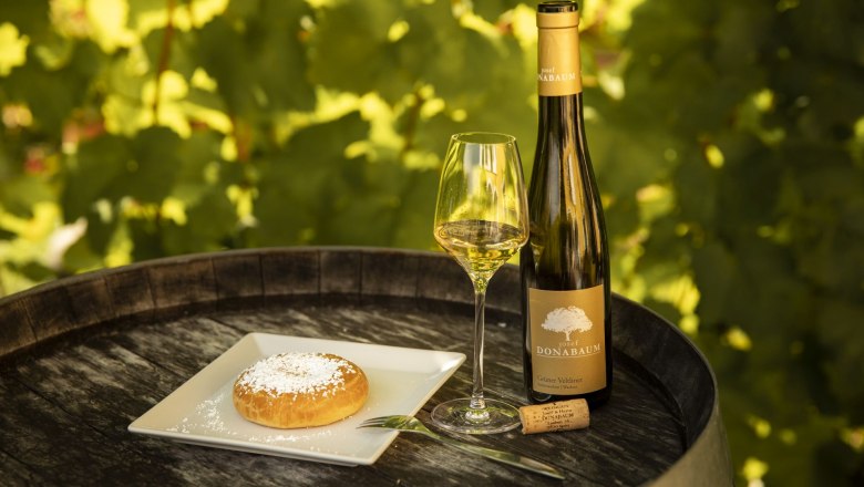 Mohnzelt_Winery Christoph Donabaum, © Nimo Zimmerhackl Wine bottle and glass with pastries on a barrel outside.