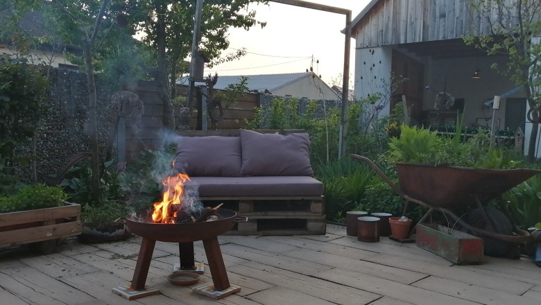 Inner courtyard, © Andrea Wiesinger A cozy courtyard with a fireplace, a sofa made from pallets and an old wheelbarrow. A wooden shed and green plants in the background.