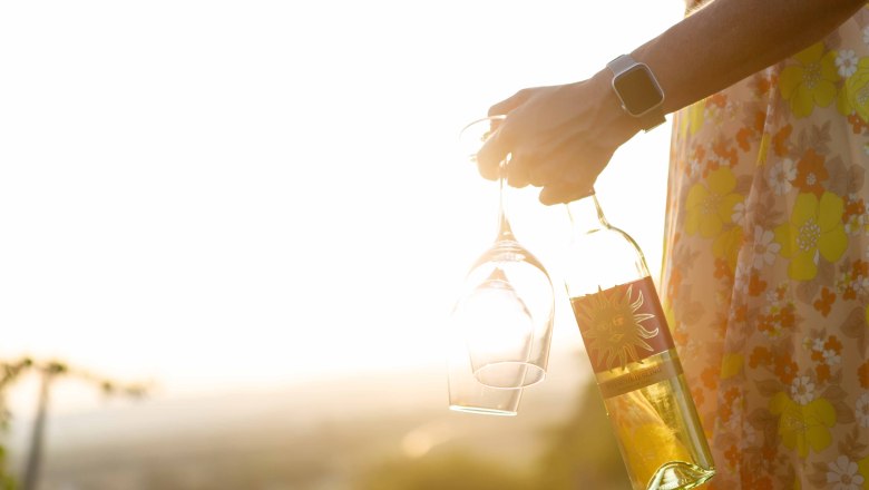 Sunset at the Sonnenhügel winery, © Astrid Bartl Person holding wine bottle and glasses in the sunset.