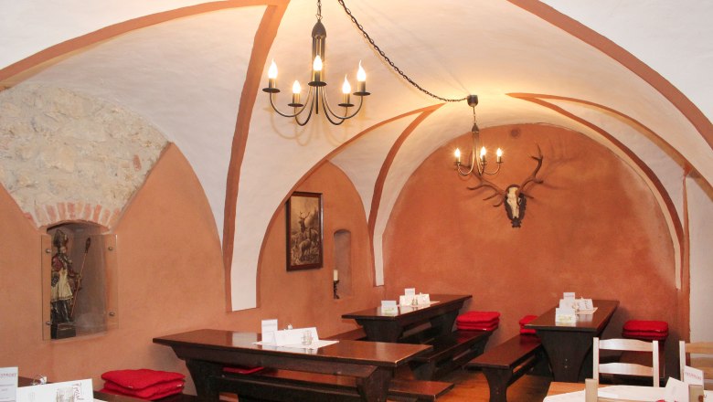 Local inside, © Weinbau Proisl Rustic restaurant with vaulted ceiling, wooden tables and deer antlers on the wall.