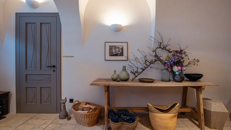 Refugium Lunz, © Niederösterreich Werbung / Maximilian Pawlikowsky Interior with wooden table, vases, flowers and baskets. Door with inscription 'shoe room'.