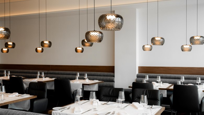 The restaurant, © Philipp Blickfang Modern restaurant with elegant hanging lamps and laid tables.