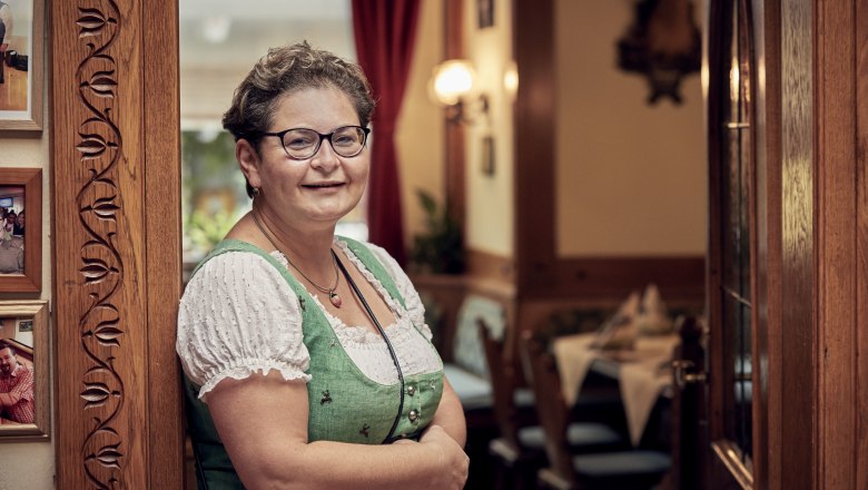 Landlady Sabine Fromwald-Karner, © Niederösterreich Werbung/Andreas Hofer A woman in traditional dress stands smiling in a cozy dining room.