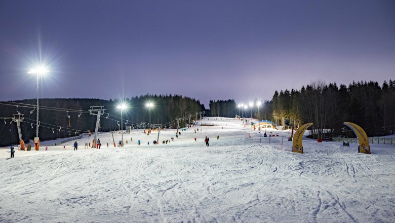 Family ski area St. Corona am Wechsel, © Stefan Wallner Illuminated ski slope in St. Corona am Wechsel with skiers and forest in the background.