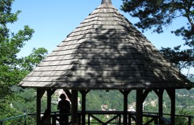 Hamerlingwarte Gars, © Wachauer A wooden pavilion with a pointed roof on a hill, surrounded by trees, overlooking a green landscape.