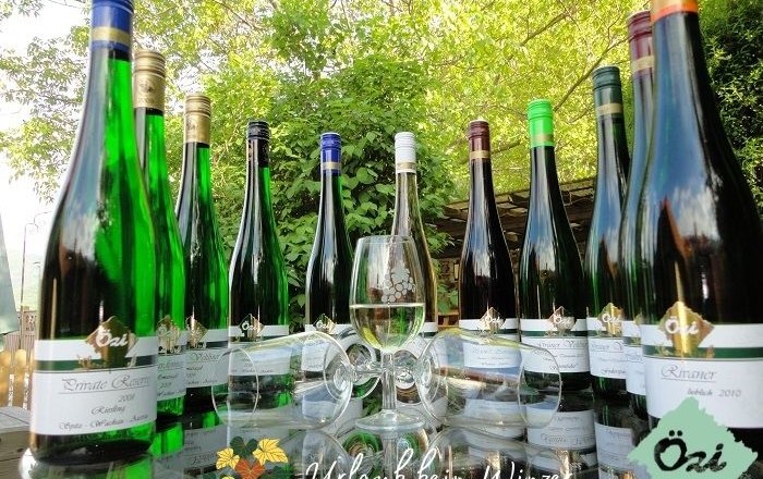 Assortment, © Özelt A selection of wine bottles and a wine glass on an outdoor table surrounded by green vegetation.