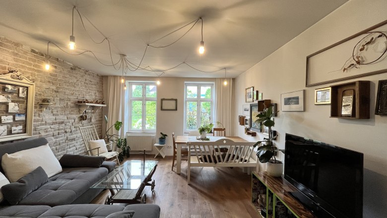 Living space, © Elisabeth Fürlinger Cozy living room with grey sofa, wooden table, plants and wall decorations.