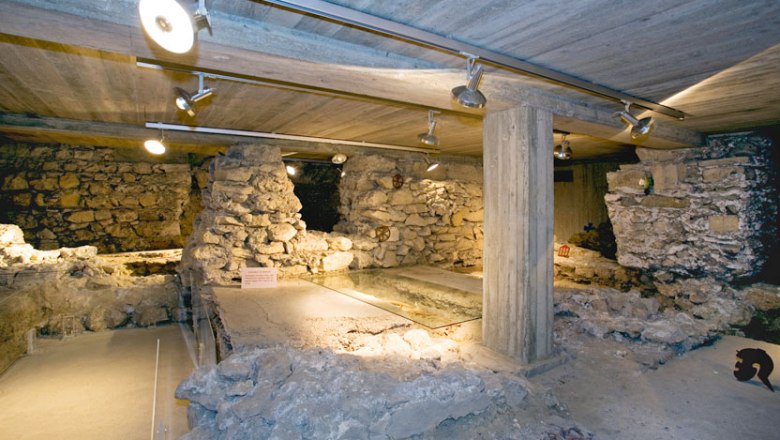 Lower church, © Stadtgemeinde Traismauer Underground ruins with stone walls and concrete pillars, illuminated by ceiling spotlights.