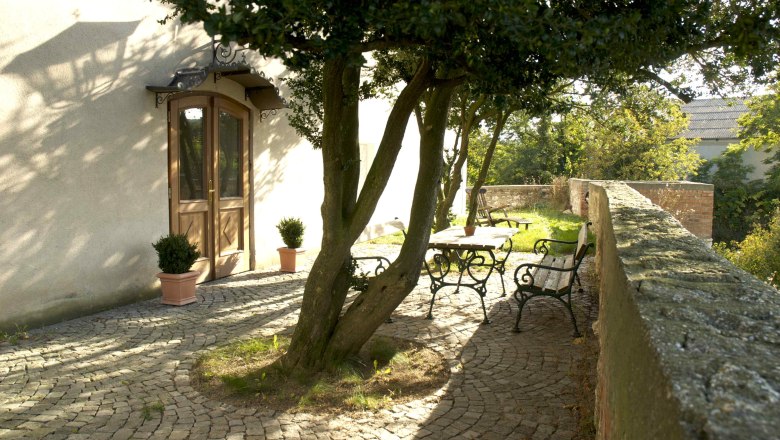 Castle terrace, © Schlosshotel Mailberg / point of view Sunny terrace with trees, wooden table and benches on cobblestones.