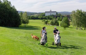 Weitra Golf Club, © www.michaelholzweber.com Two golfers with dog on a green golf course, castle in the background.