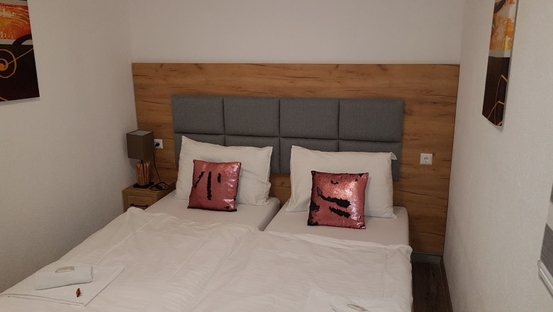 Double room, © Konrad Brandl Double room with two single beds, gray headboard, pink sequin pillows and white bed linen.