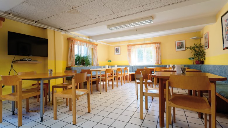 Breakfast room, © Christoph Sammer A bright breakfast room with wooden furniture, yellow walls and large windows.
