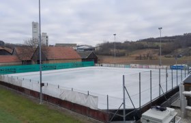 Ice rink in Sitzendorf/Schmida, © Gemeinde Sitzendorf an der Schmida An empty ice rink with surrounding buildings and hills in the background.