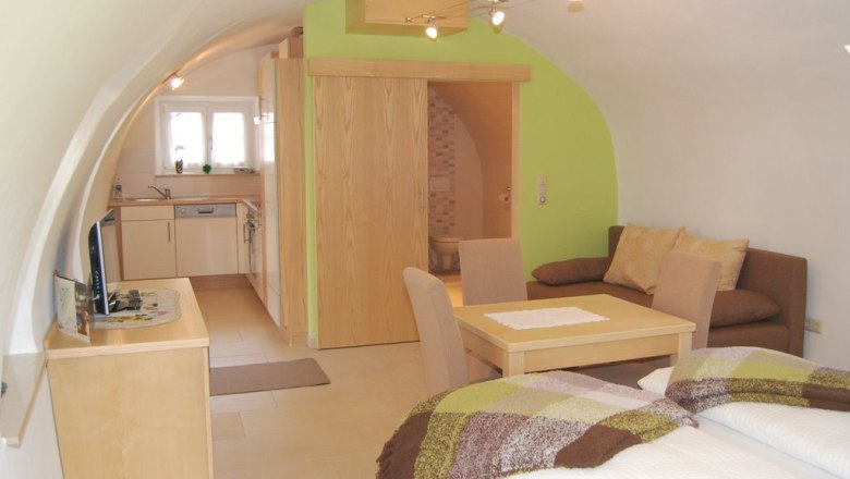 House Stierschneider, © Familie Stierschneider Cozy apartment with vaulted ceiling, kitchen, dining table, sofa and bed.