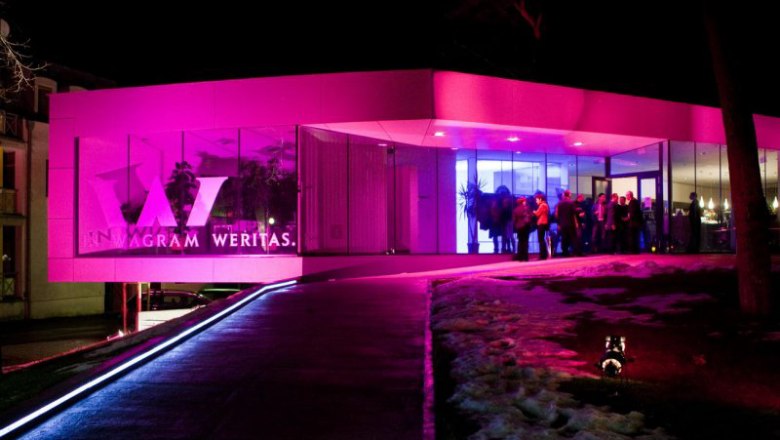 Evening atmosphere at the Weritas regional wine shop, © Gebietsvinothek Weritas Modern wine bar at night with pink lighting and people at the entrance.