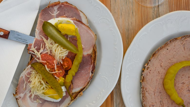 Heurigen snack, © Weinviertel Tourismus GmbH / Lisa Sedlatschek Two plates with sandwiches and two glasses of white wine on a wooden table.