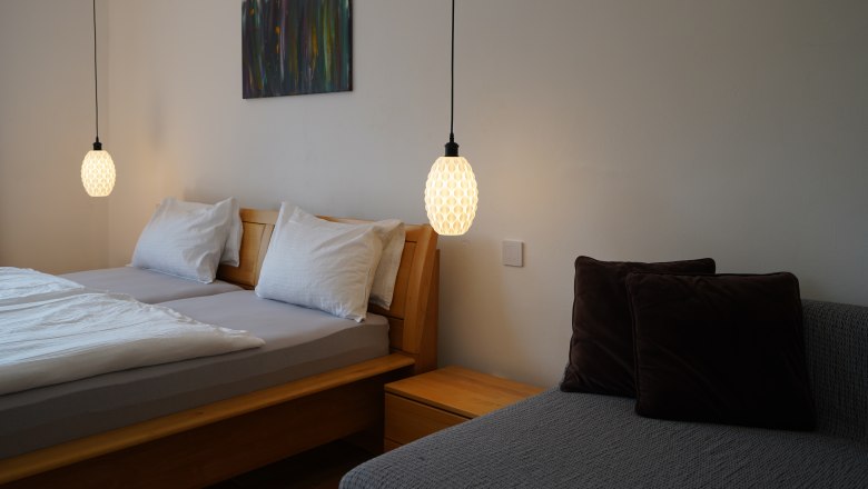 Country house Krell, © Weingut Krell Bedroom with double bed, two hanging lamps and a sofa with cushions.