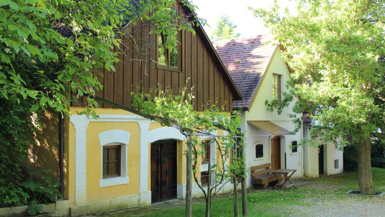 Wolkersdorf wine cellar lane, © Weinviertel Tourismus Traditional wine cellars in the wine cellar lane of Wolkersdorf, surrounded by green trees and vines.