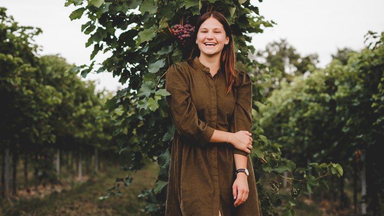 TDR-Winery Haimel, © David Schreiber A woman stands smiling in a vineyard in front of a grapevine.