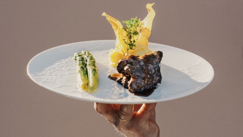 Angus beef and asparagus, © Niederösterreich Werbung/Julius Hirtzberger A plate of Angus beef, asparagus and potato chips, held by one hand.
