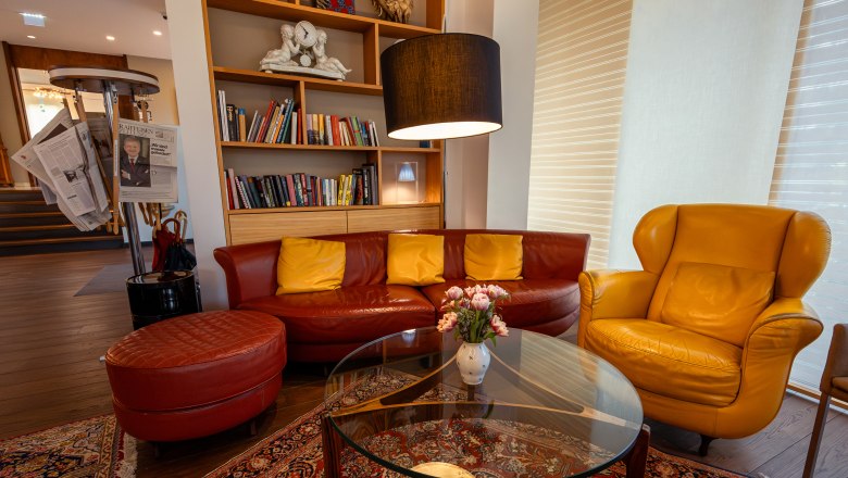 At the Park Hotel, © Niederösterreich Werbung / Maximilian Pawlikowsky Cozy hotel lobby with red and yellow leather furniture, bookshelf and newspaper rack.