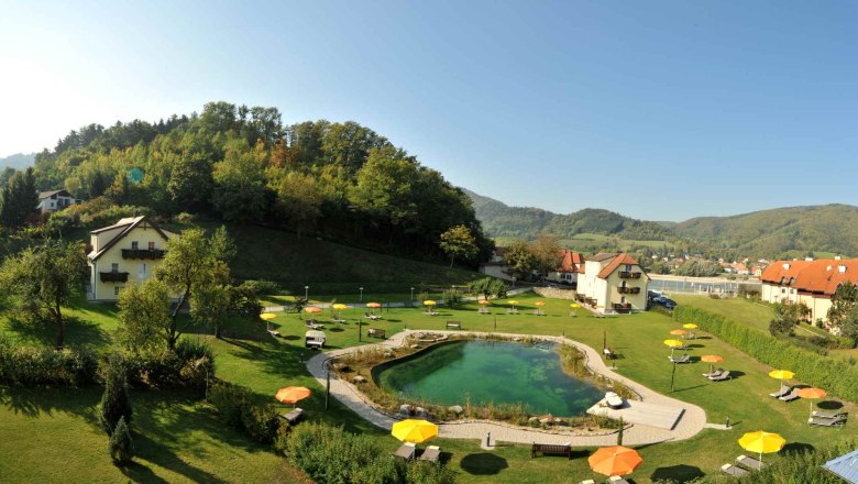 Residence Wachau - Garden, © Hotel Donauterrasse Garden area with pond, sun loungers and parasols, surrounded by hills and houses.