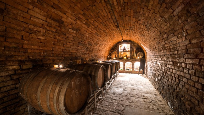 Wine barrels, © Fam. Zesch A wine cellar with wooden barrels and brick walls.